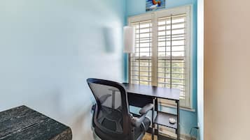 Una habitación con escritorio, silla, ventana con persianas y un cuadro en la pared.
