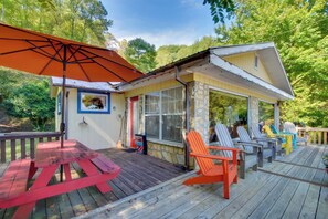 A wooden deck with a picnic table and colorful Adirondack chairs, a small covered porch, and a stone wall. - Mountain Cottage w/ Views Near Tail of the Dragon! (Fontana Dam)