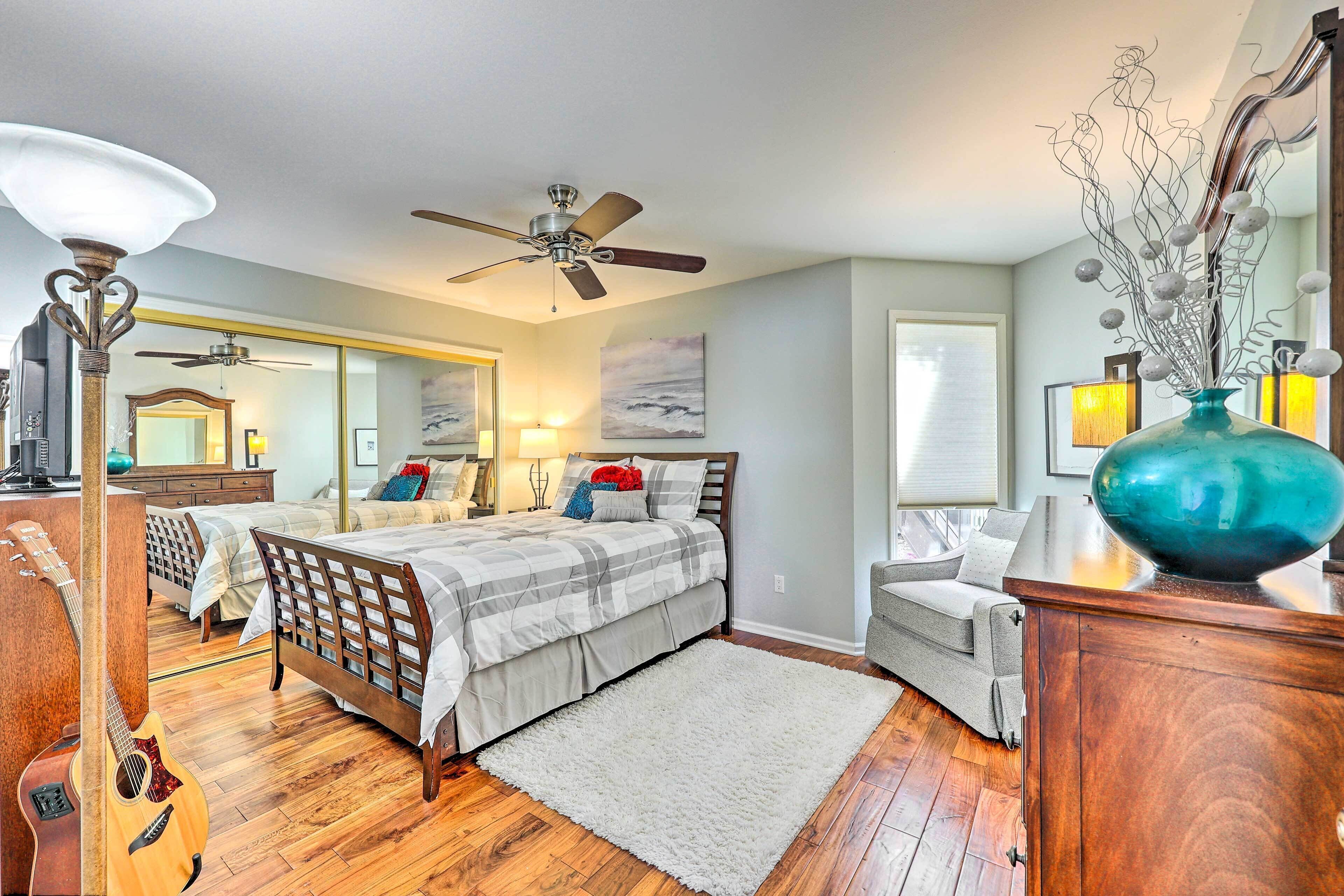 A bedroom with a bed, a dresser, a mirror, a guitar, a ceiling fan, and a vase with branches.