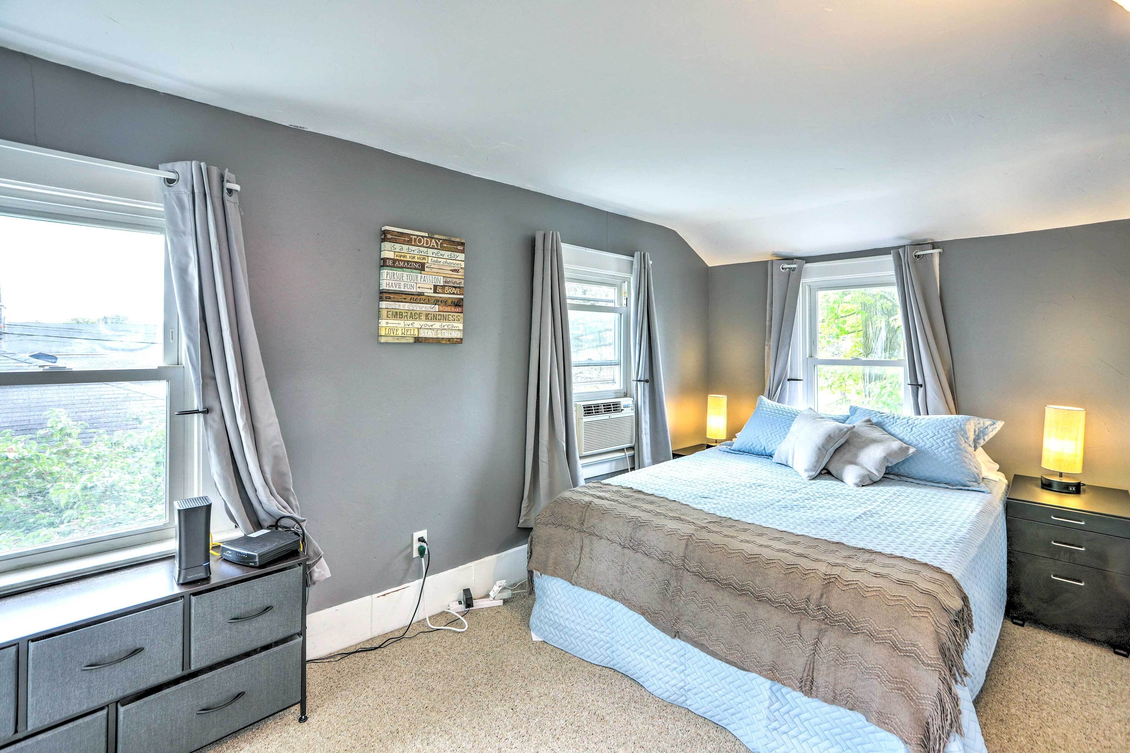 Une chambre à coucher comprenant un lit, des tables de chevet, une commode, une fenêtre avec des rideaux et un luminaire fixé au mur.