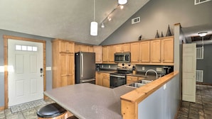A kitchen with wooden cabinets, a stainless steel refrigerator, a microwave, and a sink. - Mountain Home Cottage w/ Deck on White River! (Gassville)