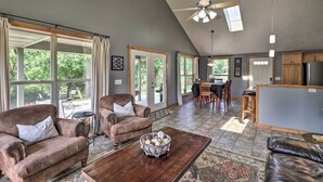 A spacious living room with leather sofas, a wooden coffee table, and a dining area with a table and chairs. - Mountain Home Cottage w/ Deck on White River! (Gassville)