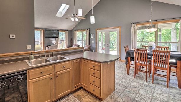 A kitchen with a large island, wooden cabinets, and a dining area with chairs and a table. - Mountain Home Cottage w/ Deck on White River! (Gassville)