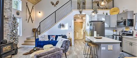 Ein geräumiger Wohnbereich mit Kamin, einem blauen Sofa, einer Holztreppe und einer Küche mit modernen Geräten.