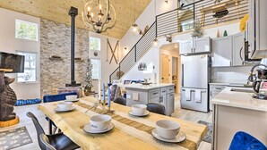A spacious dining area with a long wooden table set for four, a kitchen with modern appliances, and a staircase leading to an upper level. - 1 Mi to St Marys Glacier Trail: Modern Mtn Cabin! (Idaho Springs)