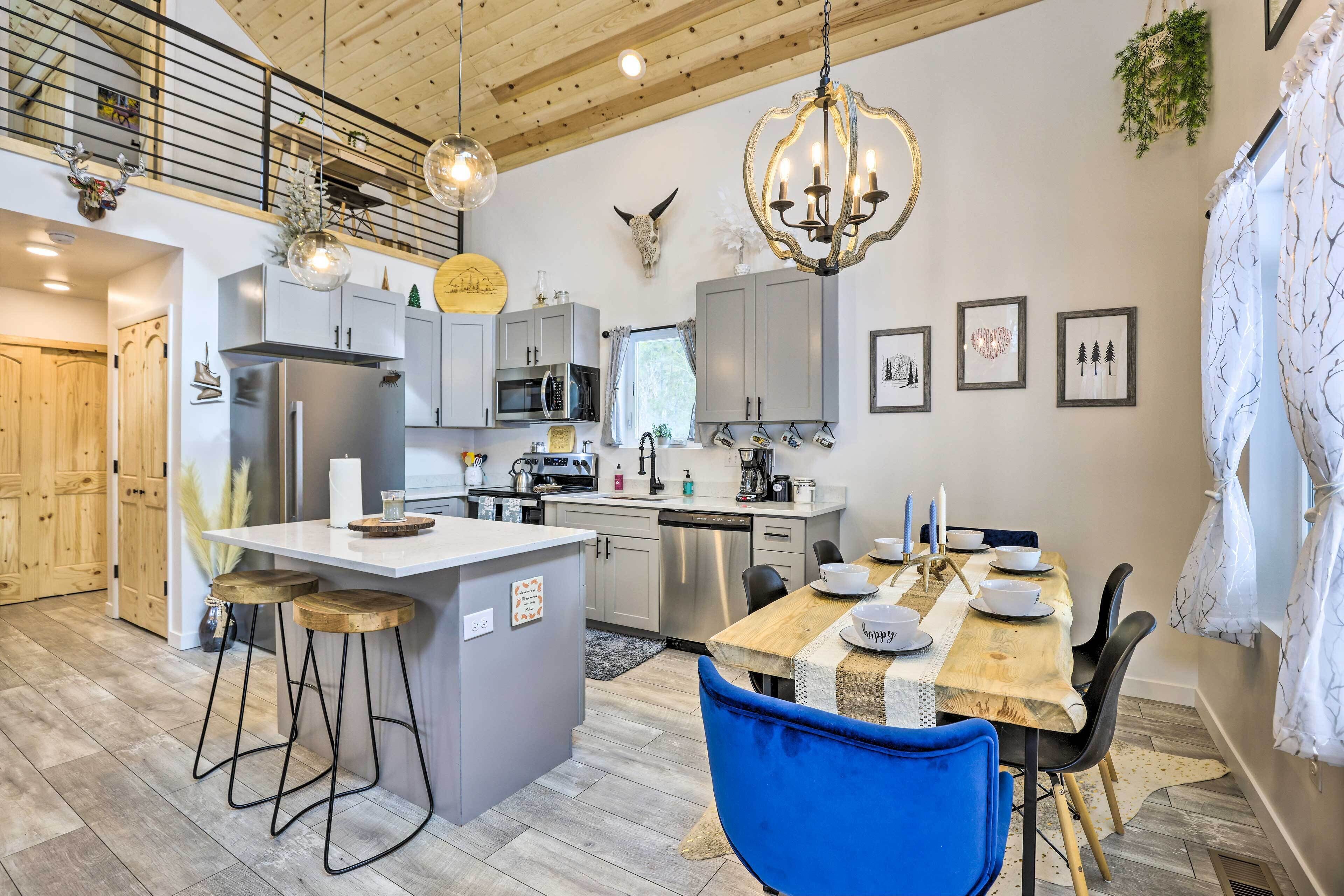 A modern kitchen with a central island, stainless steel appliances, and a dining area with a wooden table and blue chairs.