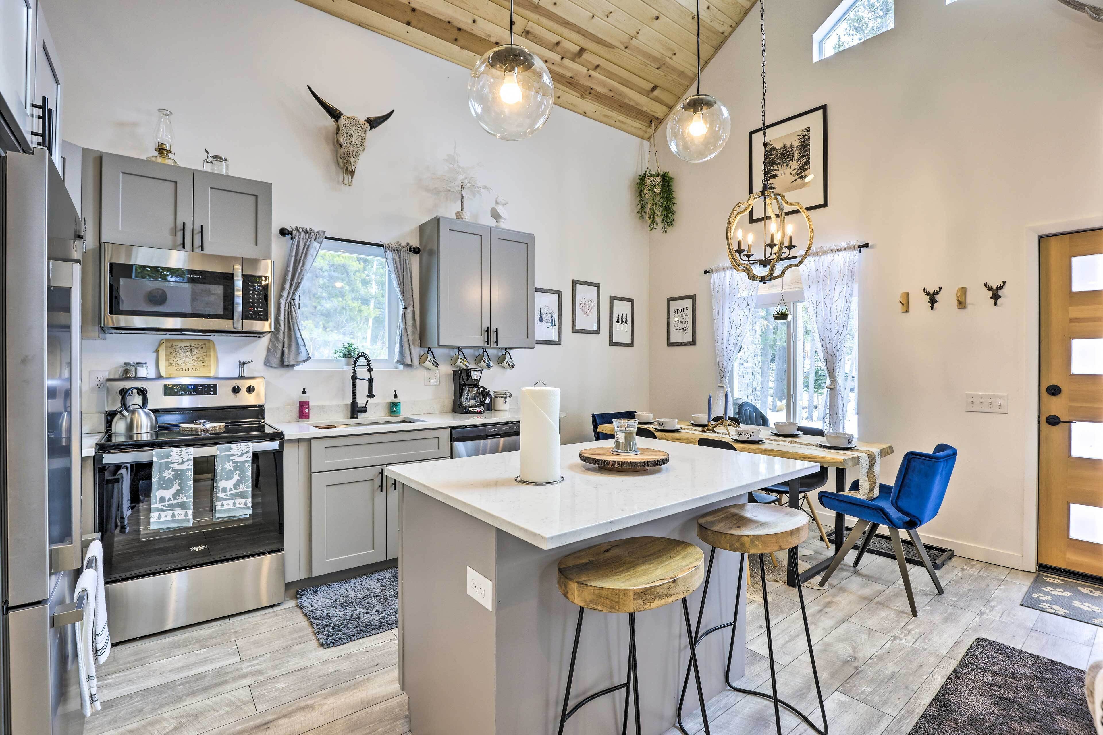 A modern kitchen with stainless steel appliances, a central island with stools, and a dining area with blue chairs.