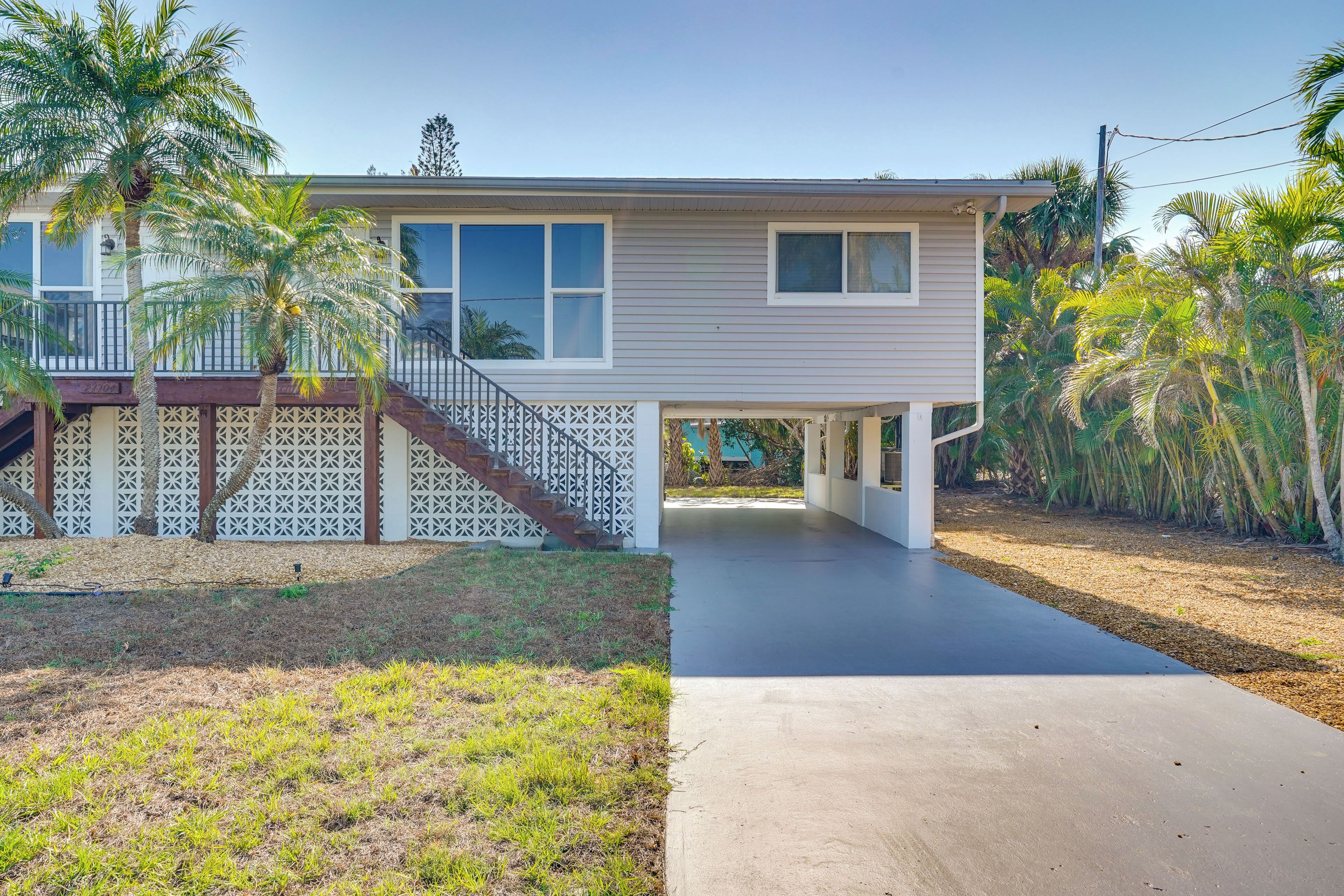 A two-story house with a covered porch, a concrete driveway, and a fenced yard with palm trees.