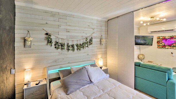 A bedroom with a bed, bedside tables, a green sofa, a wall-mounted TV, and a decorative plant arrangement. - 'the Goat Hut' Studio Casita: 11 Mi to Strip! (Las Vegas)