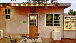 A house with a front door, two windows, a porch with a patterned rug, and a small table and chair set. - 'the Goat Hut' Studio Casita: 11 Mi to Strip! (Las Vegas)