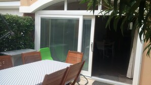 A patio with a table and chairs, a sliding glass door, and a small garden area. - APT 2 ROOMS 27m2 + TERRACE 22m2 REF 4015 (MARSEILLAN PLAGE)