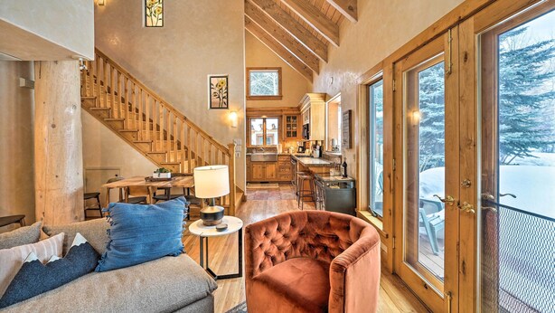 A spacious living area with a wooden staircase, a cozy seating area, and a view of a snowy landscape through large windows. - Serene Sun Valley Home w/ Hot Tub & Mtn Views (Sun Valley)