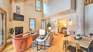 A spacious living area with a fireplace, a sofa, a dining table, and a television mounted on the wall. - Serene Sun Valley Home w/ Hot Tub & Mtn Views (Sun Valley)