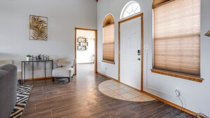 Un'ampia sala con pavimento in legno, una poltrona grigia, un tavolino con oggetti decorativi e un'opera d'arte appesa al muro.