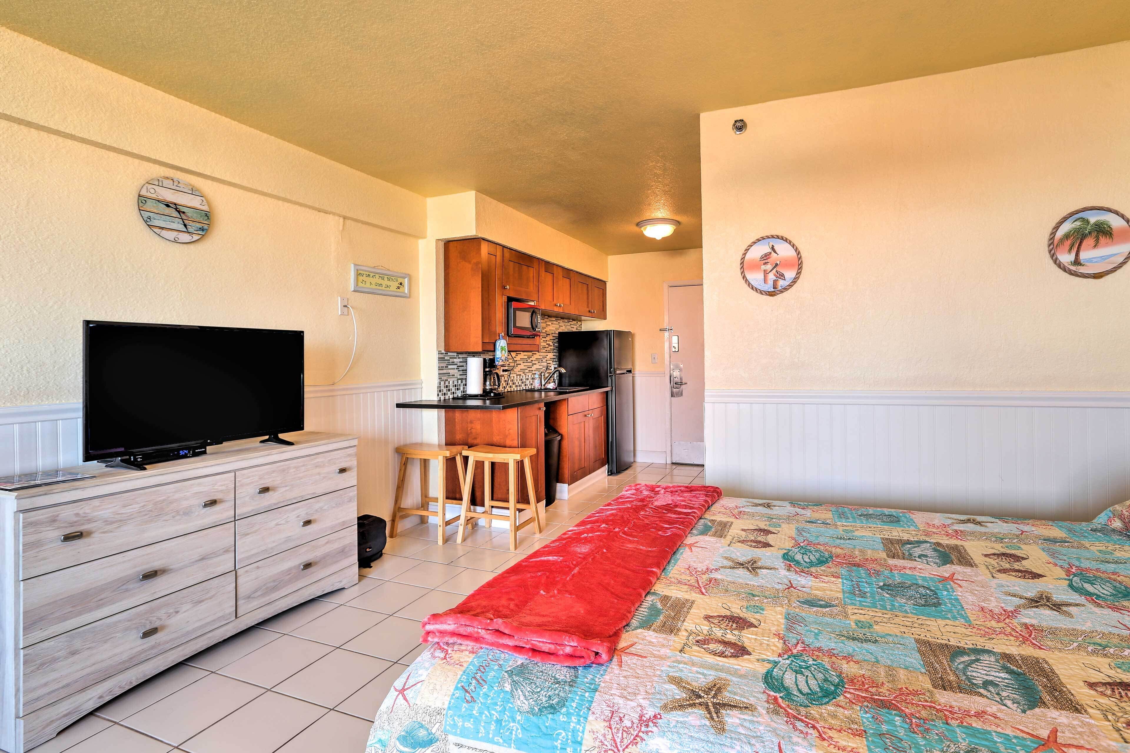 A room with a bed, a TV on a dresser, a kitchenette, and a bathroom.