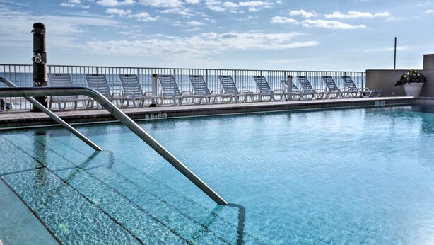 Ein Schwimmbecken mit klarem Wasser, einer Metallleiter und Liegestühlen am Rand.