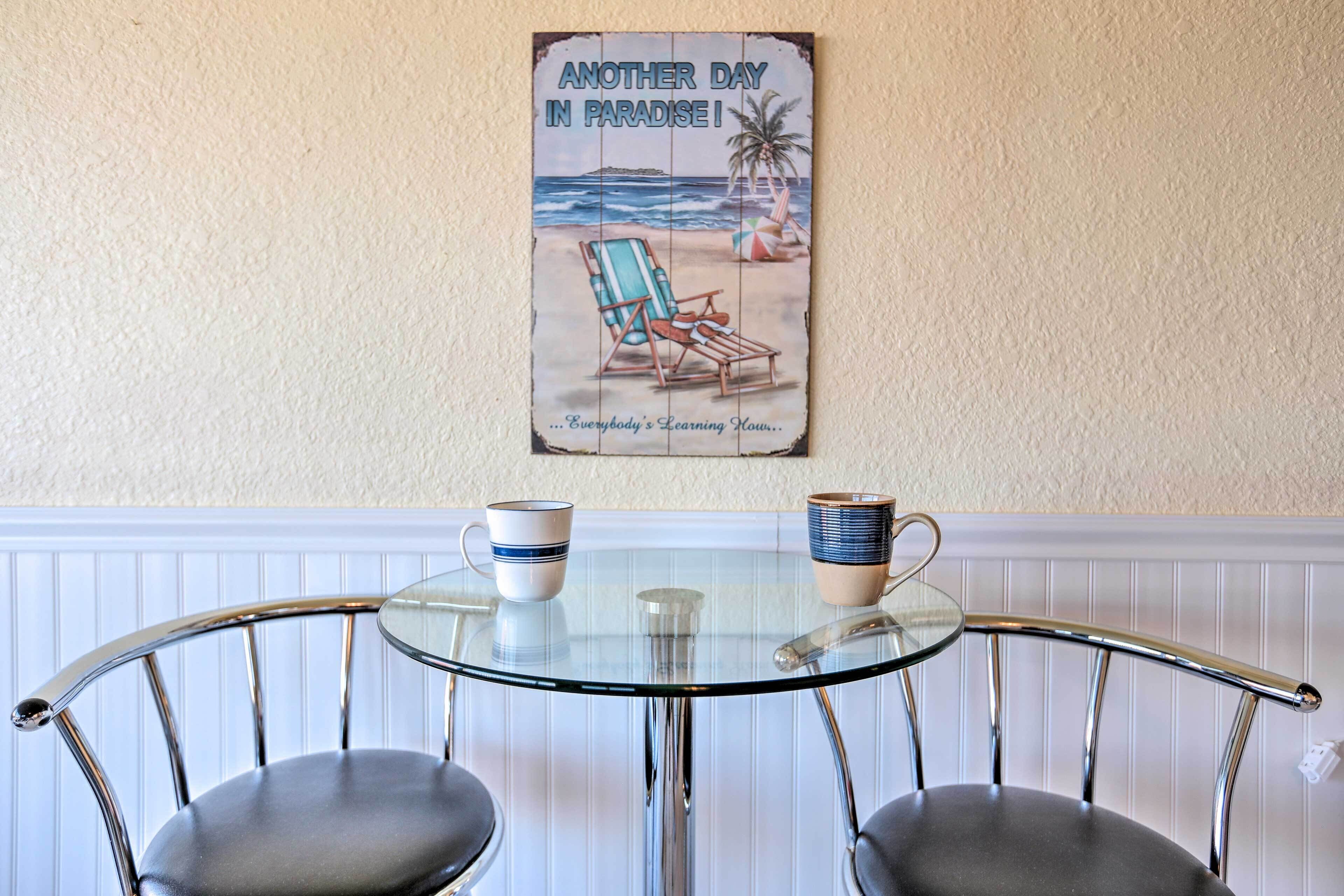 Ein Tisch mit Glasplatte, zwei Stühle, ein Poster an der Wand und zwei Tassen.