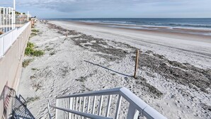 Blick auf einen Sandstrand und das Meer vom Balkon aus, inklusive Geländer.
