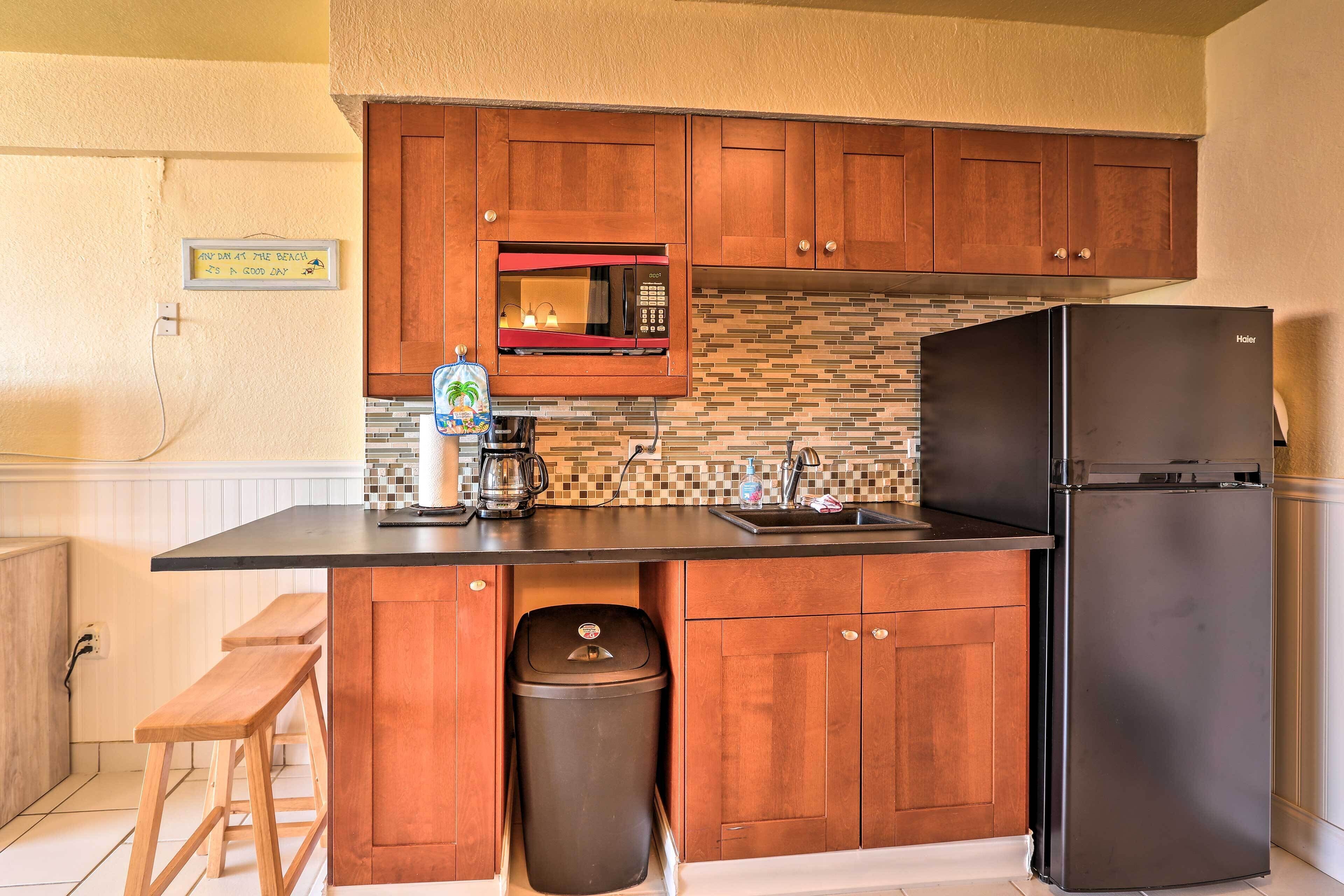 A compact kitchen with wooden cabinets, a black refrigerator, a microwave, and a coffee maker.