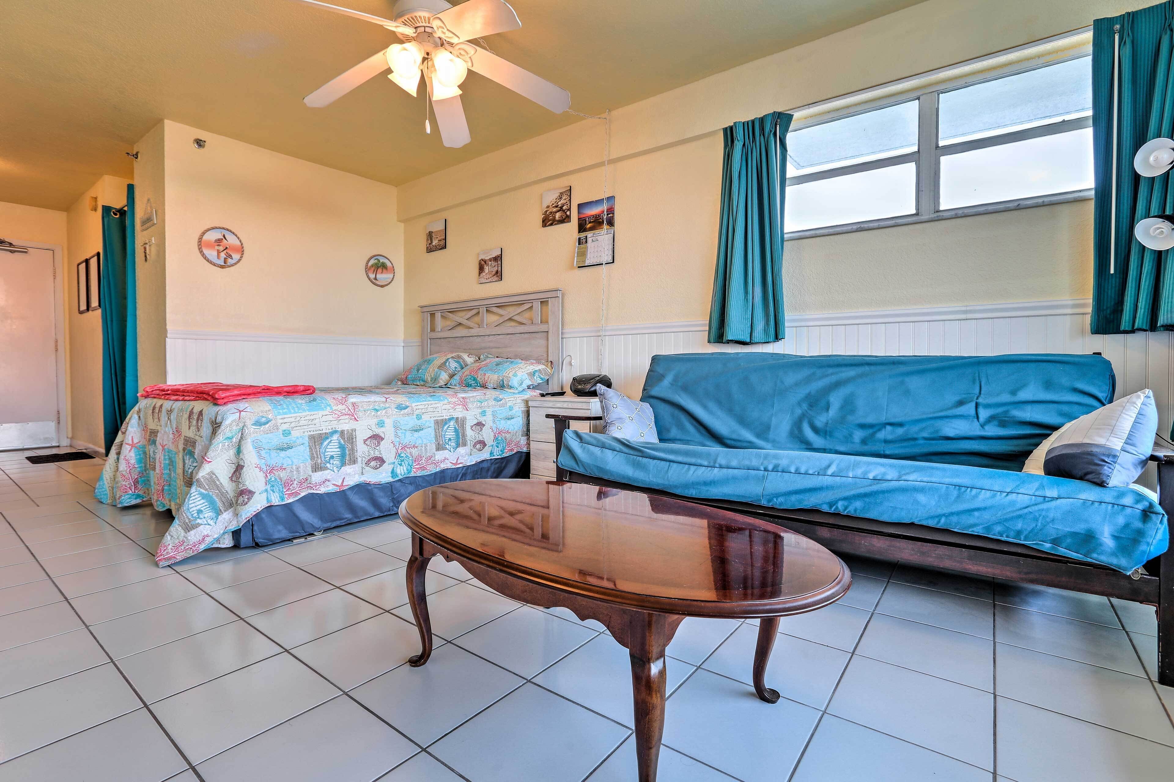 A room with a bed, a sofa, a table, and a ceiling fan.