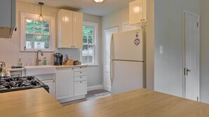 A kitchen with white cabinets, a stove, a refrigerator, and a window with a view of trees. - Charming Cincinnati Home < 10 Mi to Downtown! (Cincinnati)