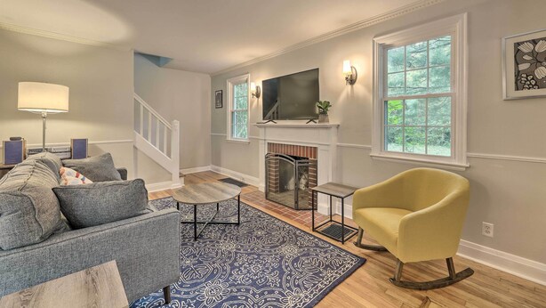 A living room with a sofa, armchair, fireplace, TV, and large windows. - Charming Cincinnati Home < 10 Mi to Downtown! (Cincinnati)