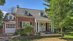 A two-story house with a brick facade, a white garage door, and a front porch with a chair. - Charming Cincinnati Home < 10 Mi to Downtown! (Cincinnati)