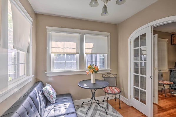 A room with a black leather sofa, a round table with a vase of flowers, and a chair with a striped cushion. - Historic Reno Home on Riverwalk: 1 Mi to Midtown (Reno)