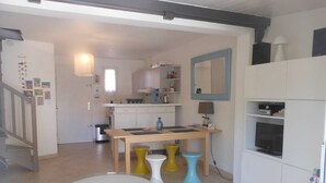A compact living space with a kitchen area, a dining table with stools, a small round table, and a television. - VILLA  3 ROOMS MEZ 47m2 + TERRACE 15m2 REF 4004 (MARSEILLAN PLAGE)