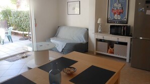 A compact living space with a sofa, a small dining table, a refrigerator, and a kitchen area with a microwave. - VILLA  3 ROOMS MEZ 47m2 + TERRACE 15m2 REF 4004 (MARSEILLAN PLAGE)