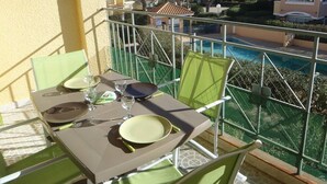 Ein Balkon mit Tisch für zwei Personen, Blick auf einen Swimmingpool und angrenzende Häuser.