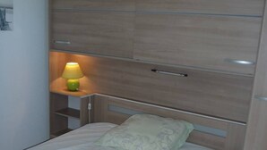 Ein Einzelbett mit Holz-Kopfteil, ein Nachttisch mit Lampe und ein an der Wand befestigtes Regal.