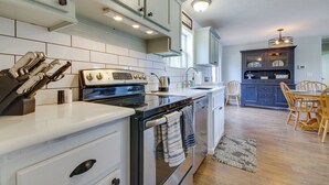 A kitchen with white cabinets, a stove, and a dining area with wooden chairs. - Gravois Mills Home: Boating Vacation! (Gravois Mills)