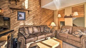 A cozy living room with a wooden sloped ceiling, two brown leather sofas with patterned cushions, a wooden coffee table, and a mounted television. - Lutsen Mountain Townhome - 2 Mi to Lake Superior! (Lutsen)