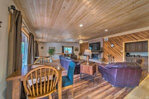 Un salon chaleureux avec un plancher en bois, un canapé en cuir, une table à manger avec des chaises et un coin cuisine doté de meubles en bois.