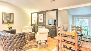Ein Wohnzimmer mit einer gepolsterten Ledersofa, einem weißen Sessel, einem Holzesstisch mit Stühlen und einer Küchenzeile mit Fernseher und Schränken.