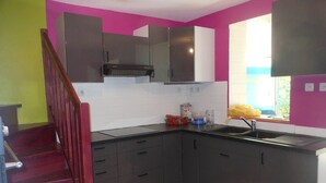 Une cuisine avec des meubles de couleur sombre, un plan de travail noir et une fenêtre équipée de stores.