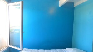 Une chambre avec un lit simple, une fenêtre et des murs bleus.