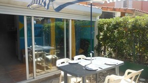 Un espace extérieur aménagé en terrasse, avec une table et des chaises, un grand parasol et une porte vitrée donnant sur un espace intérieur.
