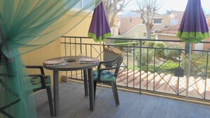 A balcony with a table and chairs, two purple umbrellas, and a view of a residential area with houses and trees.