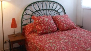 A bedroom with a green metal headboard, a floral bedspread, and a painting on the wall.