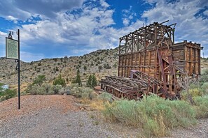 An old wooden structure with a metal framework, surrounded by dry vegetation and a clear sky.