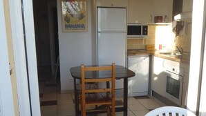 A compact kitchen with a refrigerator, microwave, and stove. There is a dining area with a table and chairs. - APT 3 ROOMS MEZ 45m2 + TERRACE 7m2 REF 4007 (MARSEILLAN PLAGE)