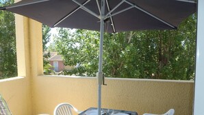 A balcony with a table set for four, white plastic chairs, and a large umbrella providing shade. - APT 3 ROOMS MEZ 45m2 + TERRACE 7m2 REF 4007 (MARSEILLAN PLAGE)