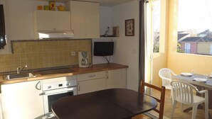 A compact kitchen with a dining area, a coffee maker, and a television on the wall. - APT 3 ROOMS MEZ 45m2 + TERRACE 7m2 REF 4007 (MARSEILLAN PLAGE)
