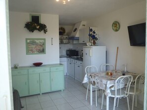 Functional kitchen and dining area with a refrigerator, microwave, and sink, adjacent to a dining table with white chairs.