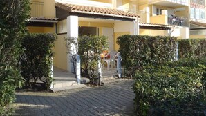 A yellow building with a tiled roof, a covered entrance, and a paved pathway. - APT 3 ROOMS 35m2 + TERRACE 13m2 REF 4010 (MARSEILLAN PLAGE)