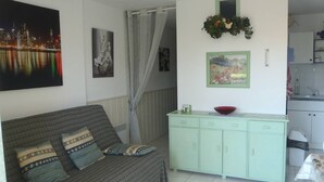 A living room with a sofa, a cabinet, and a painting of a cityscape. - APT 3 ROOMS 35m2 + TERRACE 13m2 REF 4010 (MARSEILLAN PLAGE)