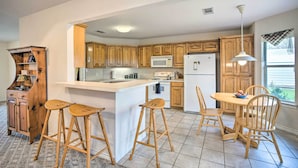 A kitchen with wooden cabinets, a white refrigerator, a microwave, a stove, and a dining area with wooden chairs and stools. - Family Alba Home w/ Boat Dock on Lake Fork! (Alba)