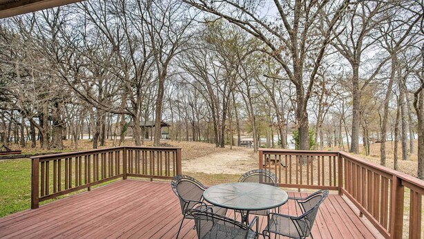 A wooden deck with a round table and chairs, surrounded by a wooden railing, overlooking a wooded area. - Family Alba Home w/ Boat Dock on Lake Fork! (Alba)